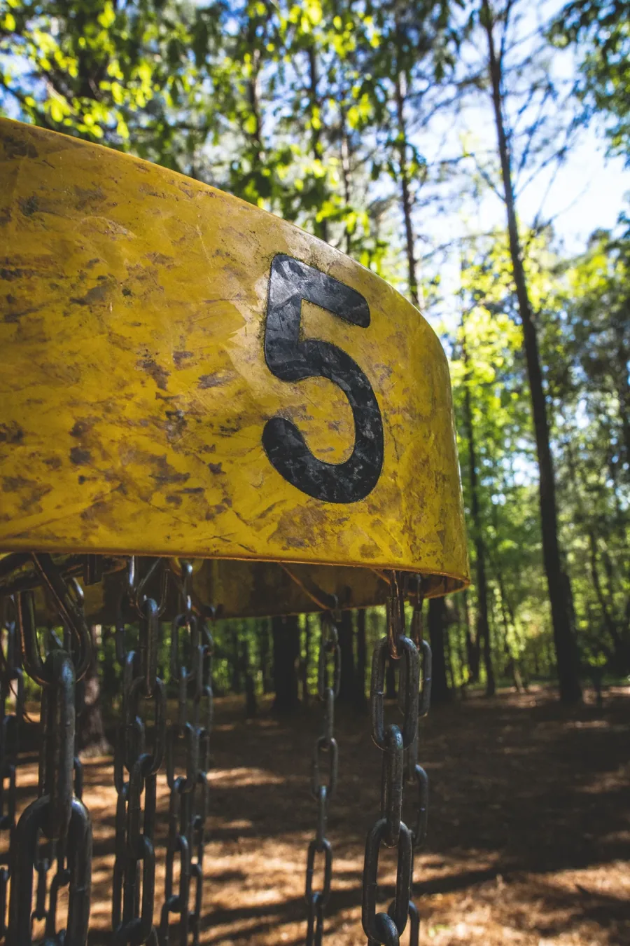 A real yellow disc golf basket photographed among sunlit trees in Lawrenceville, Georgia